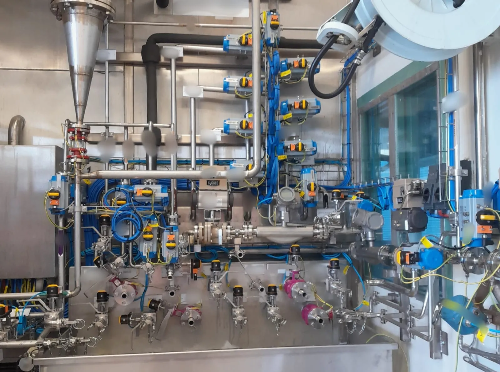 Ruostumattomasta teräksestä valmistettu teollisuuslaitteisto, jossa on putkia, venttiilejä ja johtoja, kirkkaassa valaistuksessa.